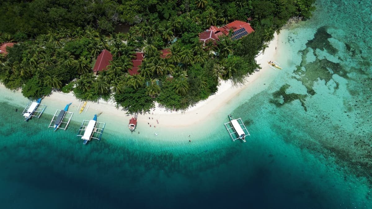 Outrigger boats and swimmers at a sand spit seen from directly above