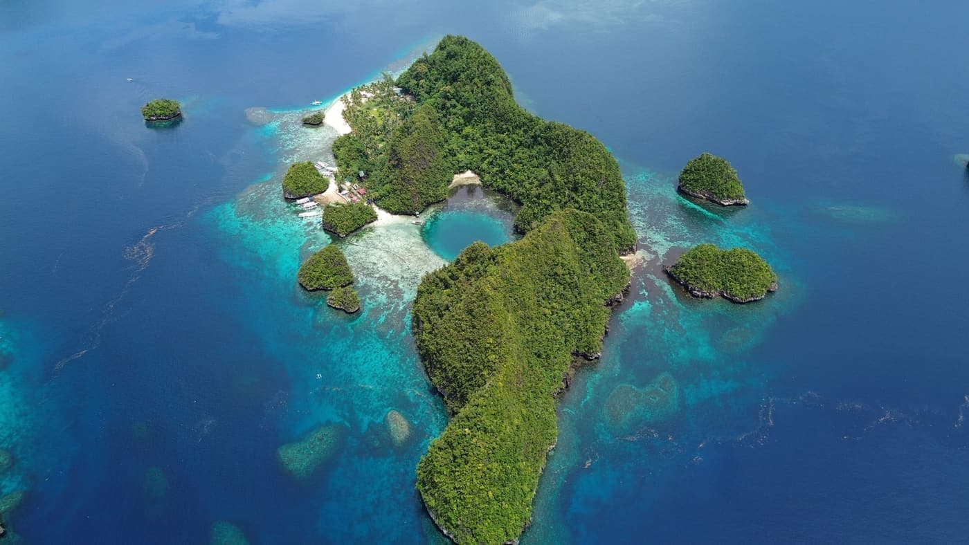An island in Libjo ringed by shallow turquoise reef, photographed from the air