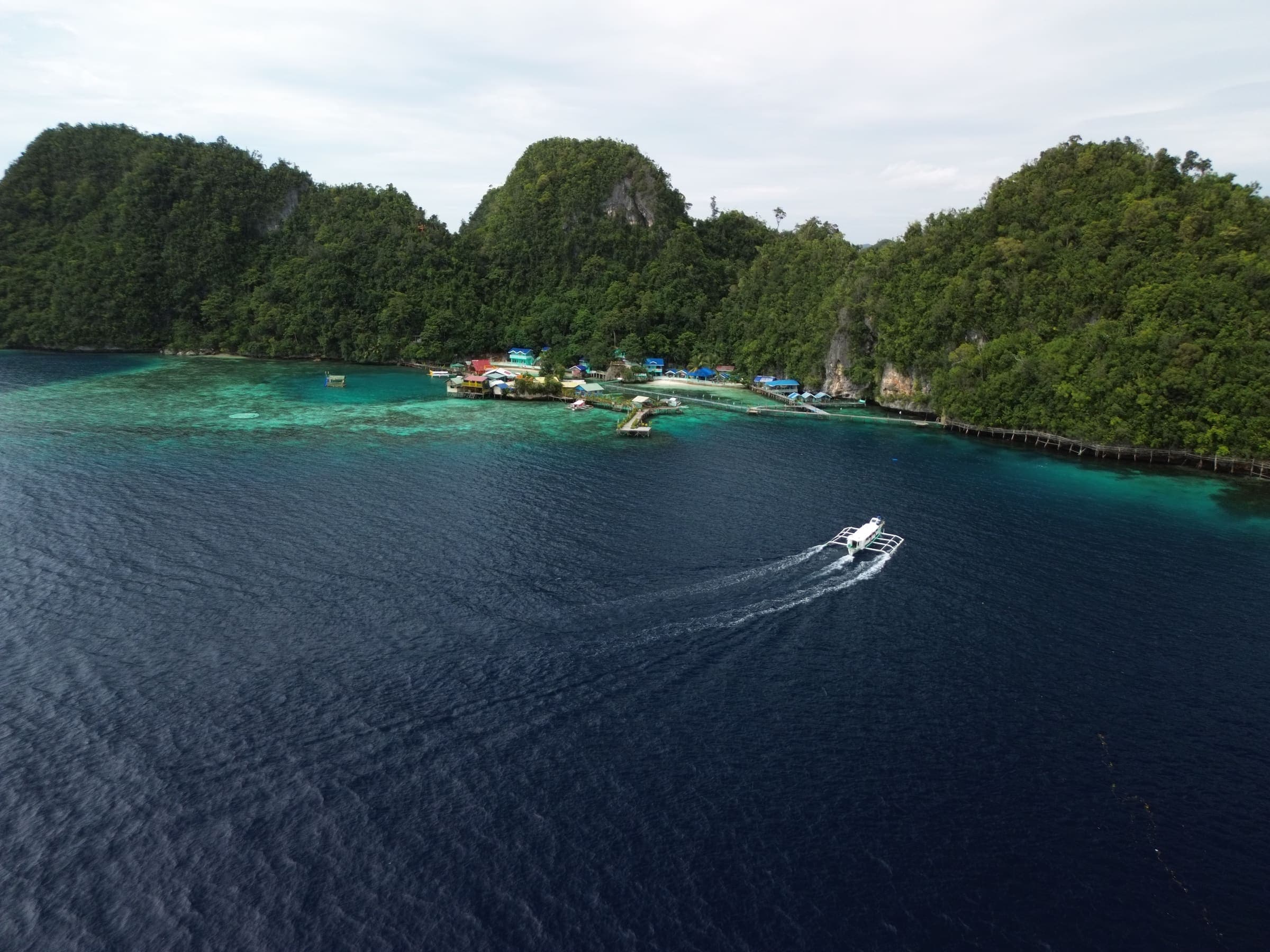 A tour boat under way across open water toward a small island community backed by limestone cliffs in Dinagat