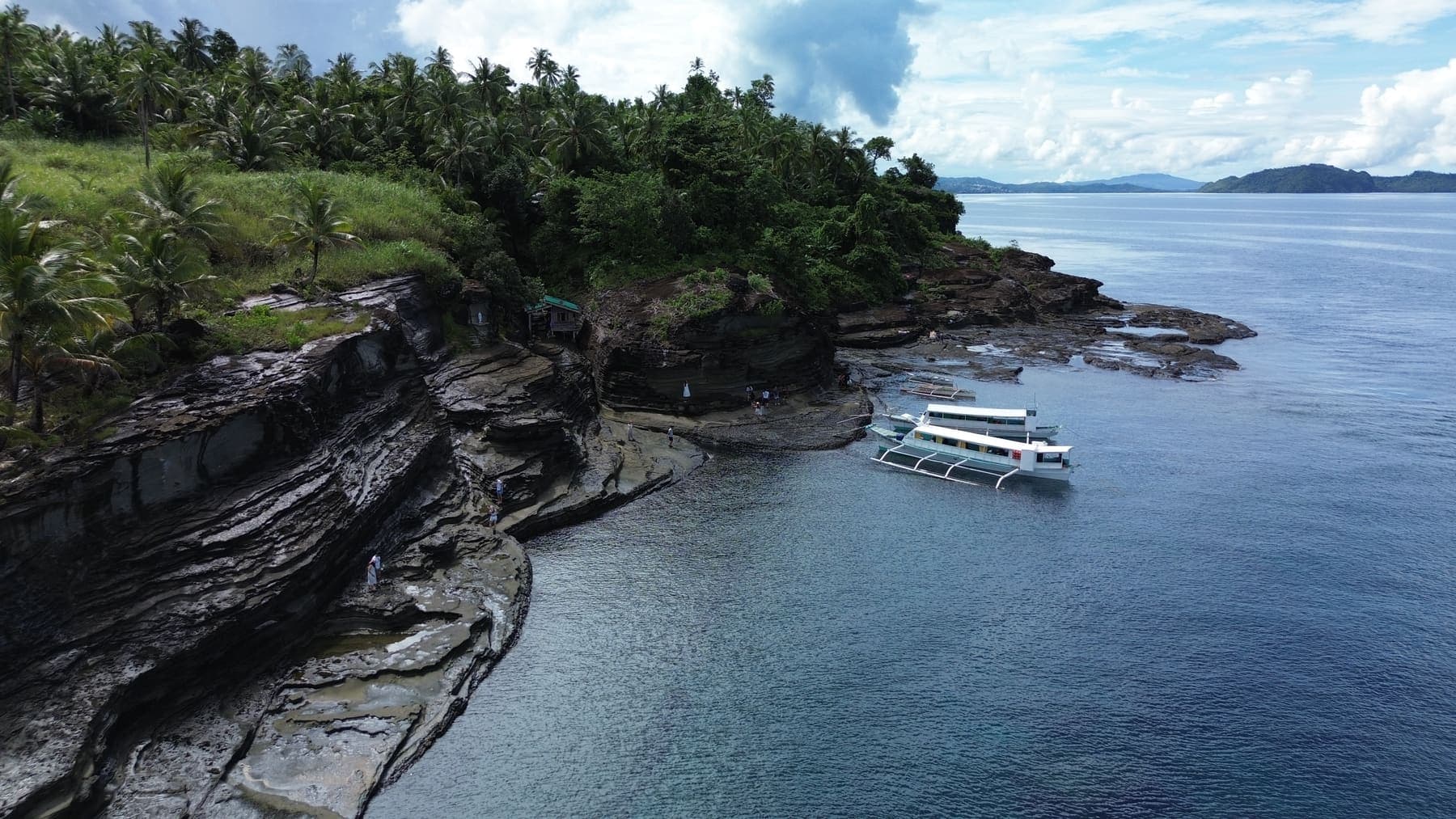 An outrigger boat moored against a rocky shore below coconut palms in Dinagat