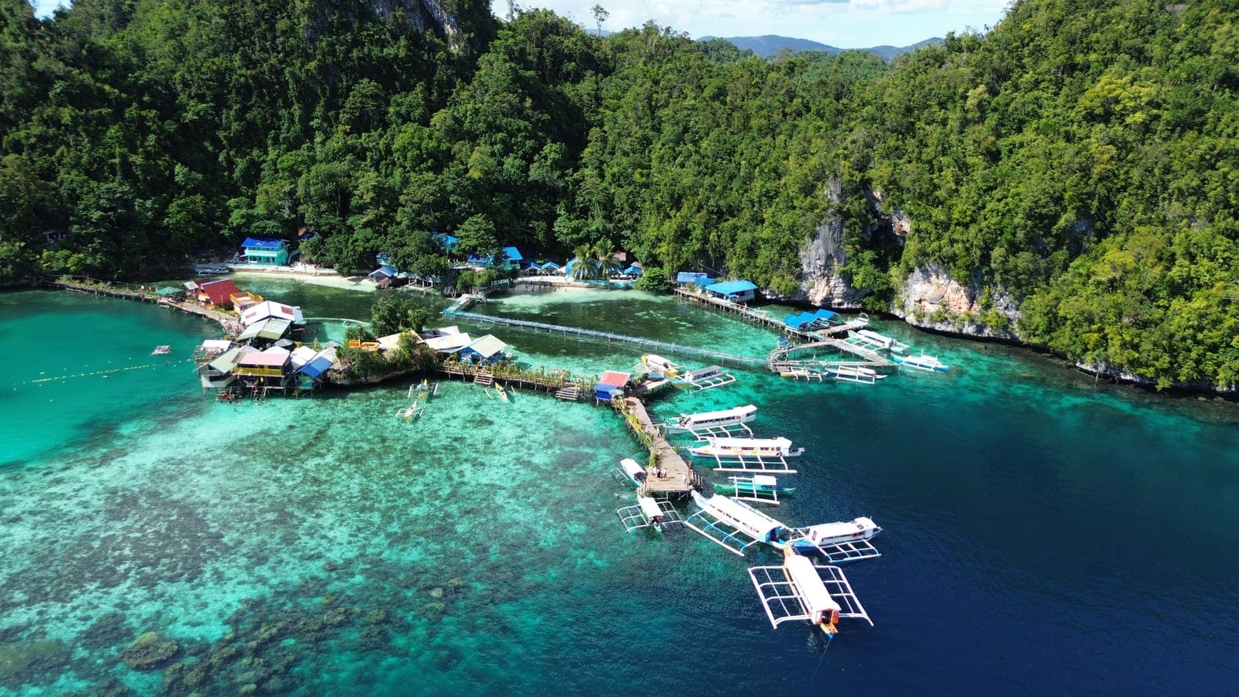 Outrigger boats gathered off a small island community with clear reef beneath them