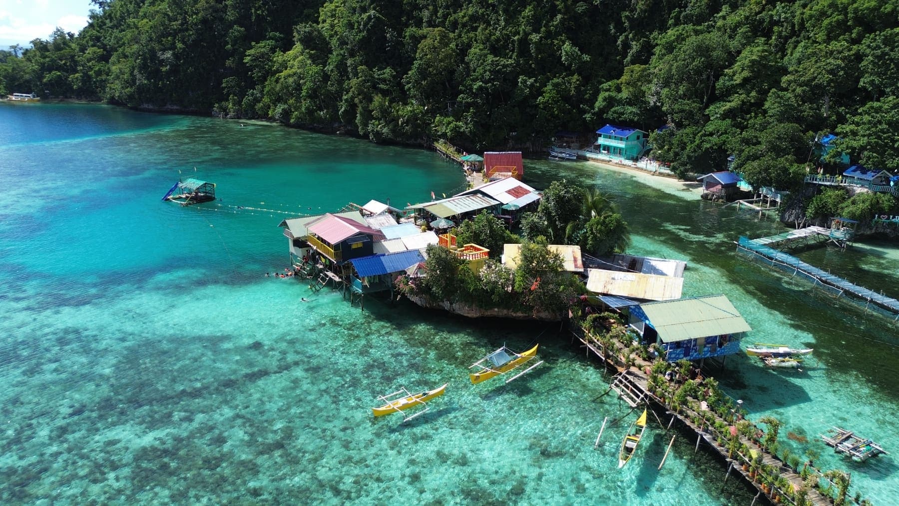 Stilt huts and small buildings at the water's edge on Jelmars islet, above clear reef
