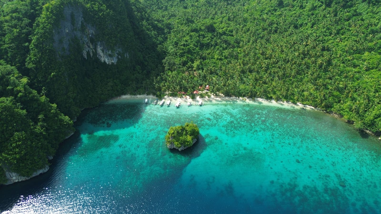 A cove on Dinagat Islands with a small forested islet standing in shallow reef water off the beach