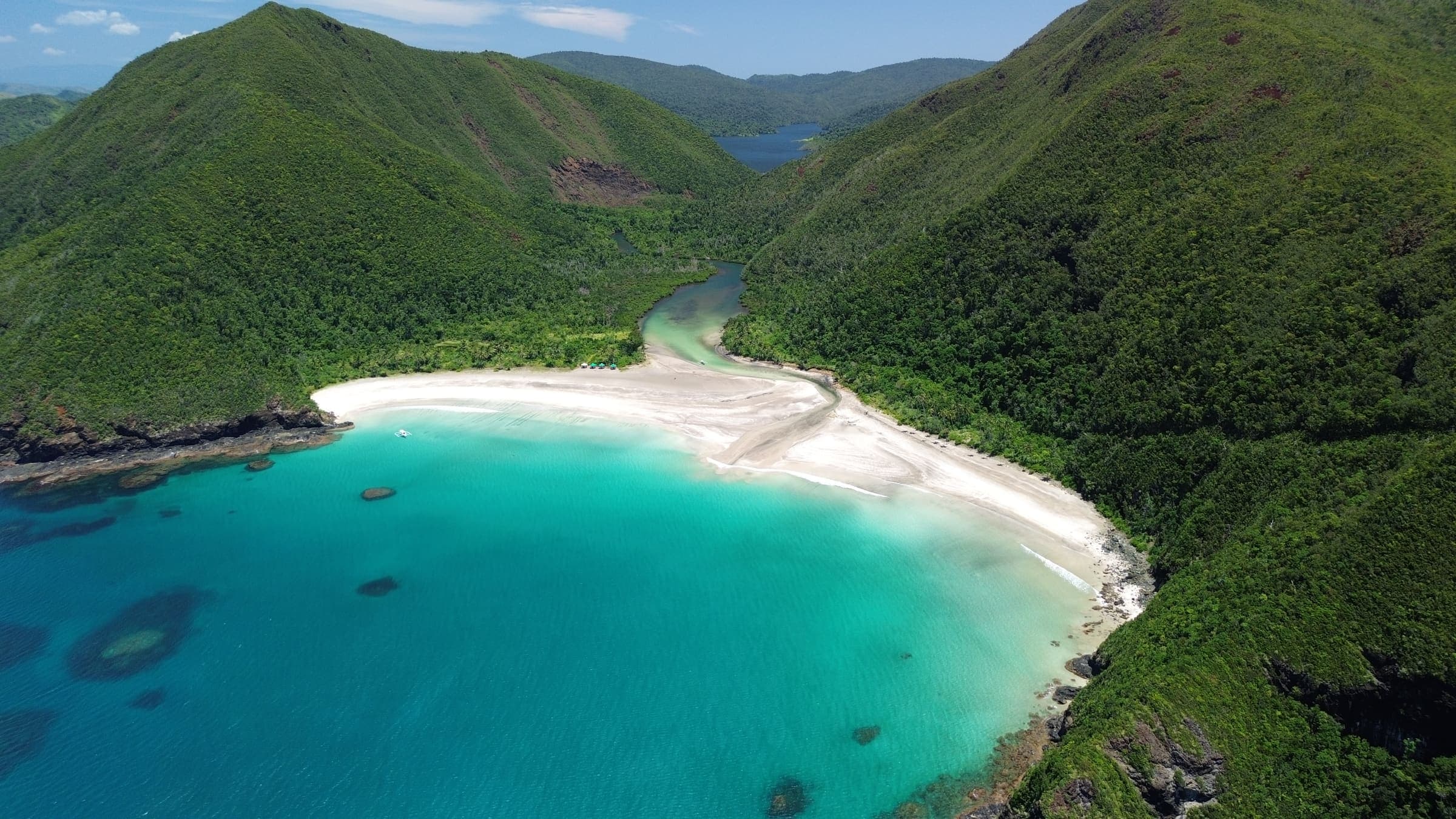 A wide white beach on Dinagat Islands enclosed by green headlands, with clear turquoise water running along the shore