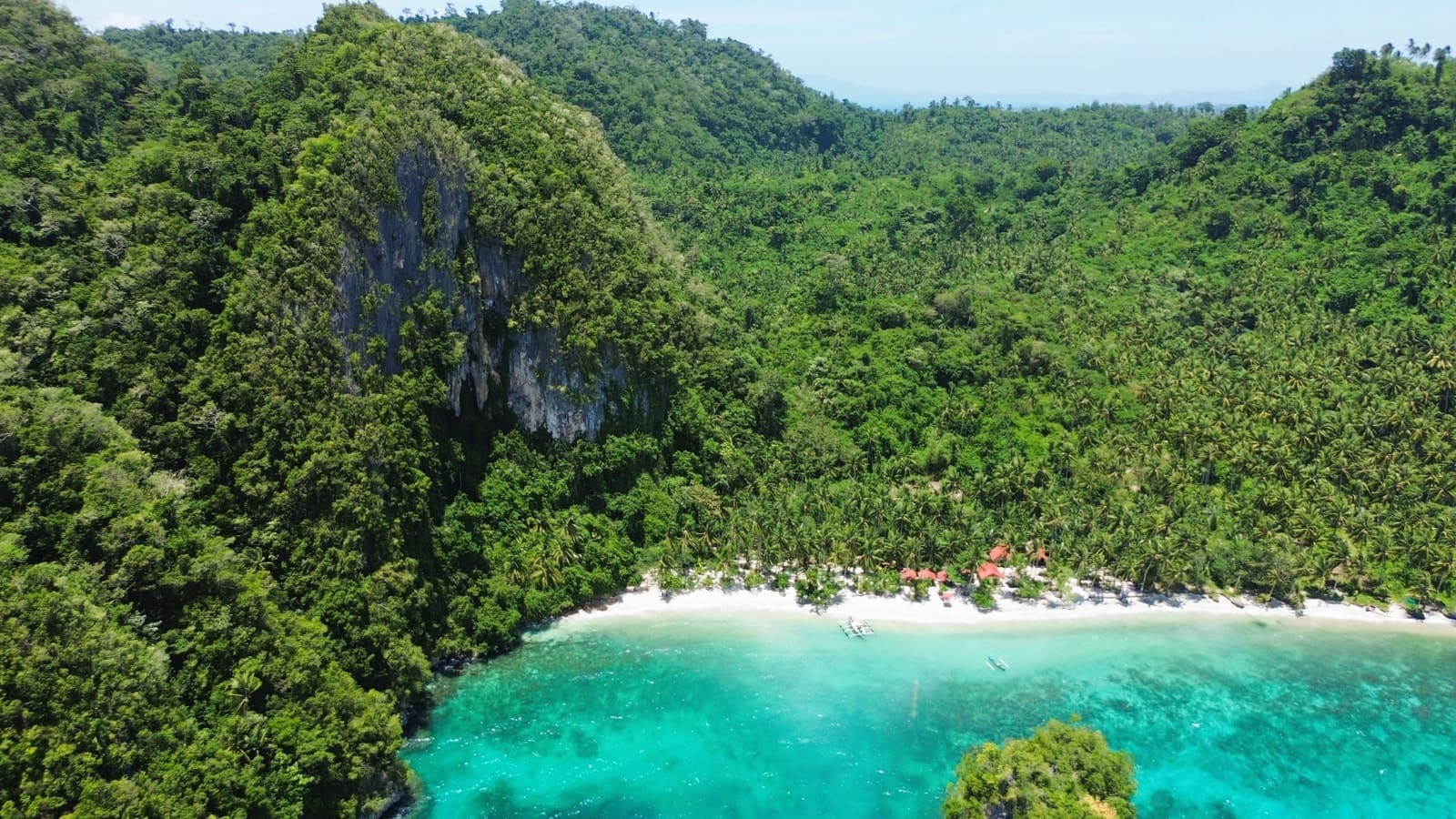 Cabacungan Cove seen from above: a crescent of white sand at the foot of a steep limestone hill
