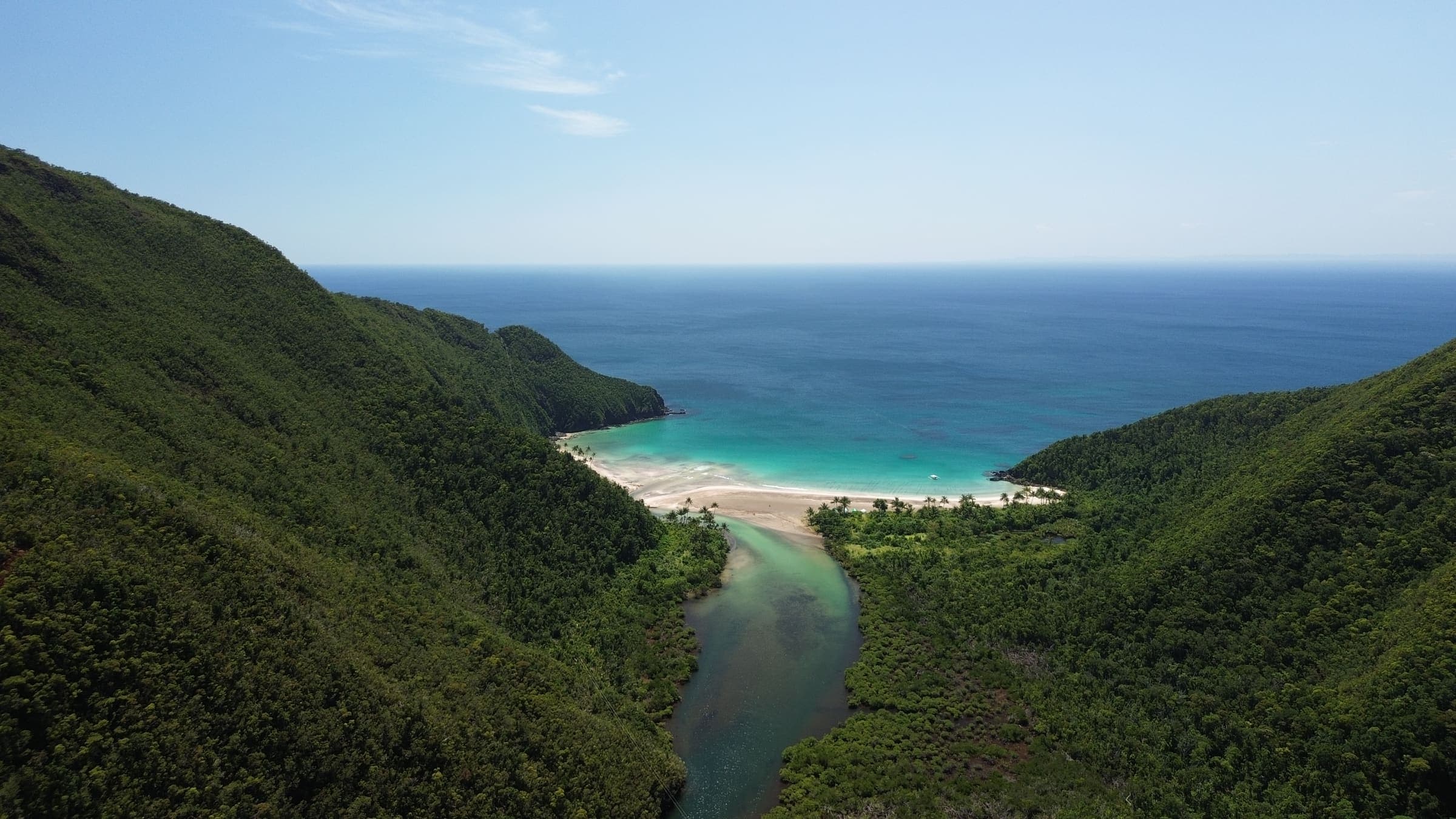 Aerial view of a forested valley in Dinagat Islands opening onto a curved white beach and the open Pacific beyond
